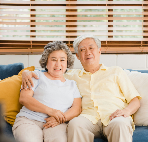 Image of older couple smiling and sitting on a couch.