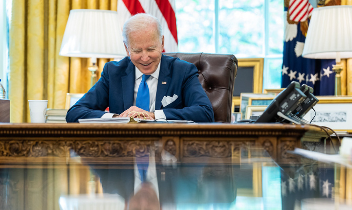 President Biden smiles while sitting at his desk