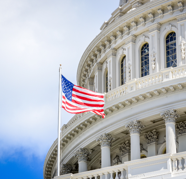 Image of federal building with blue sky background and american flag blowing in the wind.