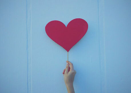 Hand holding a paper heart on a stick.